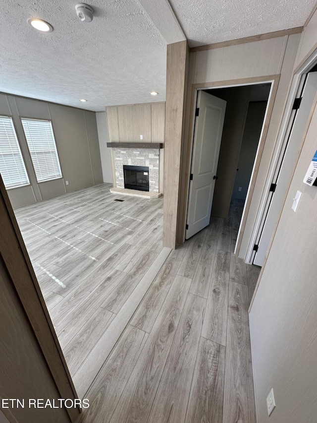 unfurnished living room featuring a stone fireplace, a textured ceiling, and light hardwood / wood-style flooring