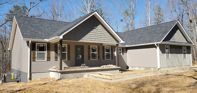 view of front facade with covered porch, a shingled roof, and cooling unit