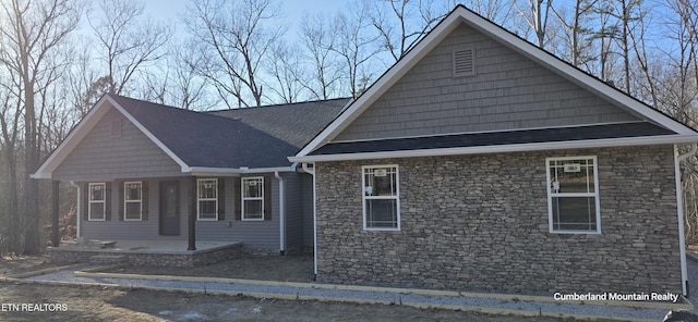 view of front facade featuring stone siding, roof with shingles, and covered porch