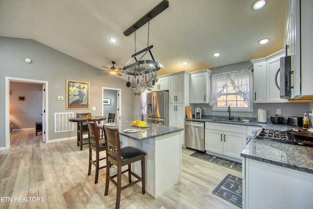 kitchen featuring sink, a kitchen island, lofted ceiling, white cabinets, and appliances with stainless steel finishes