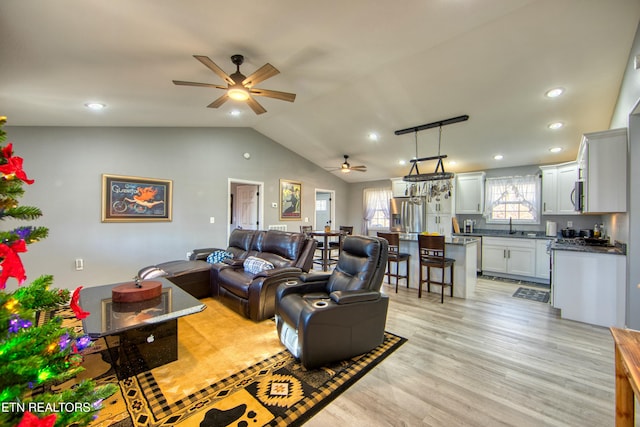 living room with ceiling fan, light wood-type flooring, sink, and vaulted ceiling