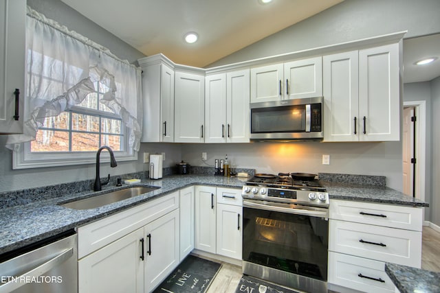 kitchen featuring stainless steel appliances, vaulted ceiling, sink, dark stone countertops, and white cabinets