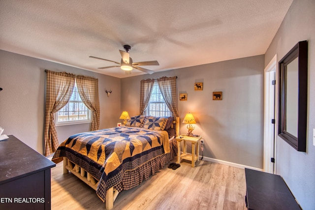 bedroom with ceiling fan, light wood-type flooring, a textured ceiling, and multiple windows