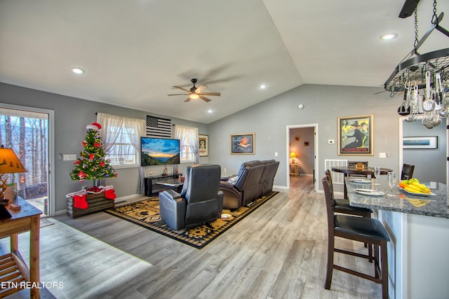 living room with ceiling fan, vaulted ceiling, and light wood-type flooring