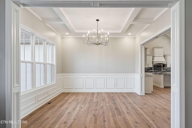 unfurnished dining area with light hardwood / wood-style flooring, a chandelier, and coffered ceiling