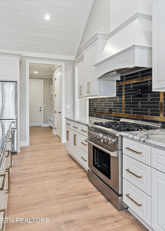 kitchen featuring appliances with stainless steel finishes, light wood-type flooring, premium range hood, light stone counters, and white cabinetry