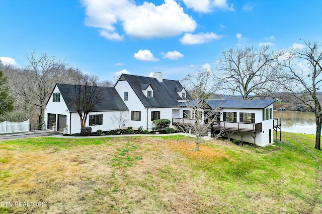 back of house featuring a deck with water view, a garage, and a lawn