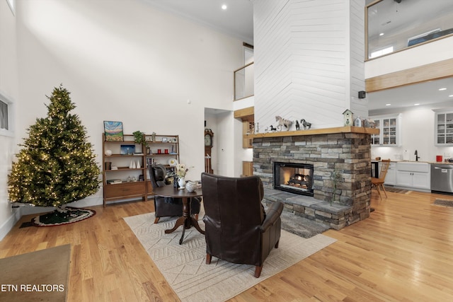 living room featuring a high ceiling, light wood-type flooring, a stone fireplace, and sink