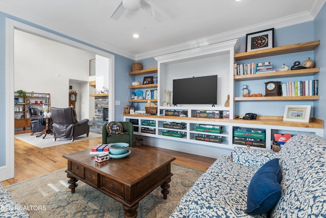 living room with ceiling fan, a stone fireplace, wood-type flooring, and ornamental molding