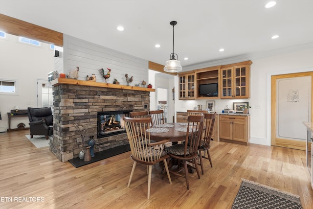 dining area featuring a stone fireplace, crown molding, and light wood-type flooring