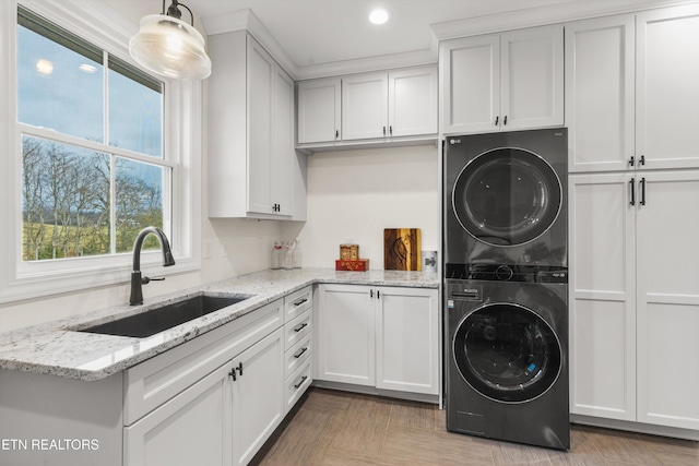 clothes washing area with cabinets, sink, stacked washer / dryer, and light parquet flooring