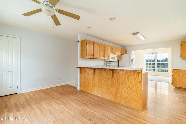 kitchen with ceiling fan with notable chandelier, white appliances, sink, light hardwood / wood-style flooring, and a breakfast bar area