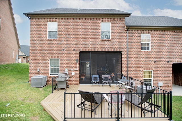 rear view of property featuring a lawn, a sunroom, a wooden deck, and central AC