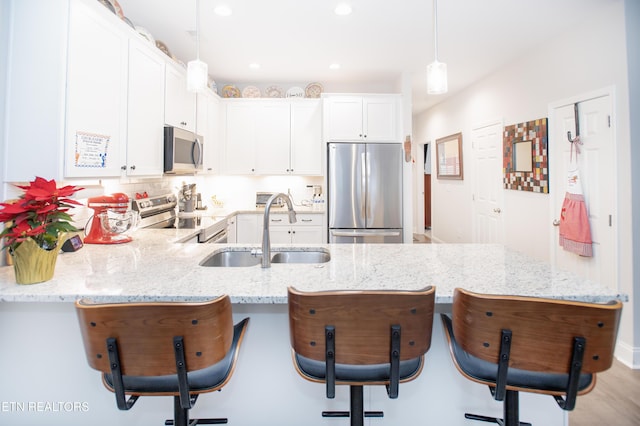 kitchen featuring kitchen peninsula, appliances with stainless steel finishes, sink, decorative light fixtures, and white cabinetry