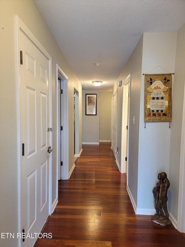 hallway with a textured ceiling and dark wood-type flooring