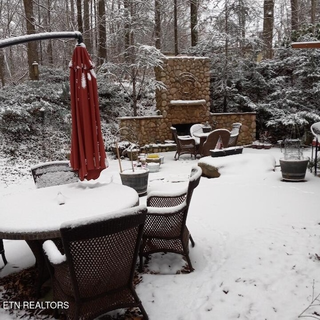 snow covered patio with an outdoor stone fireplace