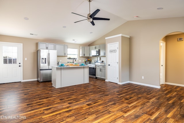 kitchen featuring appliances with stainless steel finishes, ceiling fan, dark wood-type flooring, a center island, and lofted ceiling