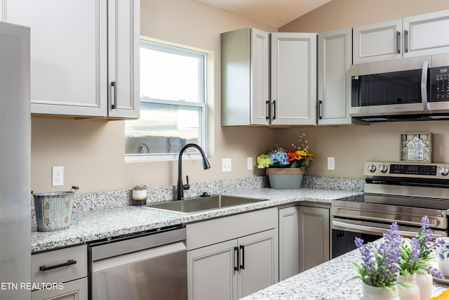 kitchen featuring light stone countertops, appliances with stainless steel finishes, lofted ceiling, and sink