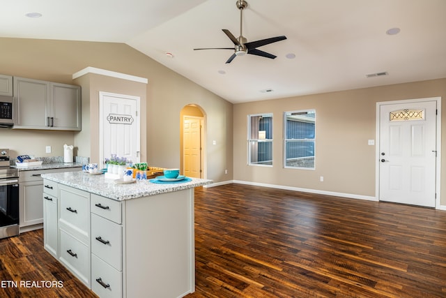 kitchen featuring light stone countertops, ceiling fan, dark wood-type flooring, a kitchen island, and appliances with stainless steel finishes