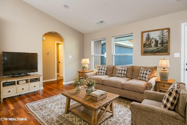 living area featuring dark wood-type flooring, visible vents, baseboards, arched walkways, and lofted ceiling