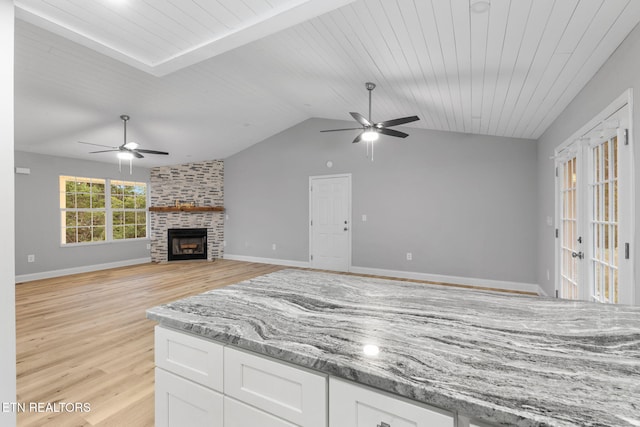 kitchen featuring light stone countertops, ceiling fan, a stone fireplace, and white cabinetry