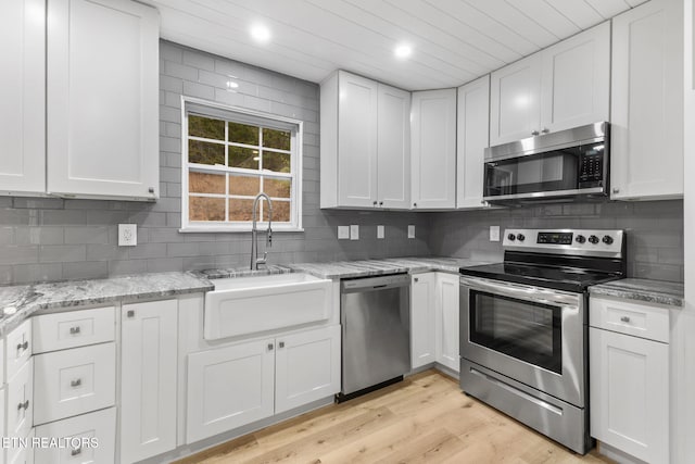 kitchen featuring appliances with stainless steel finishes, tasteful backsplash, sink, white cabinets, and light hardwood / wood-style floors