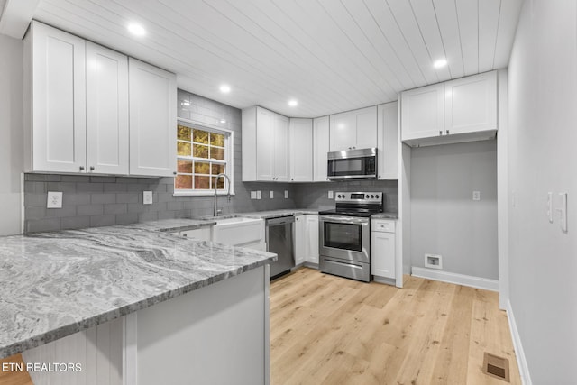 kitchen featuring kitchen peninsula, light stone counters, stainless steel appliances, light hardwood / wood-style flooring, and white cabinets