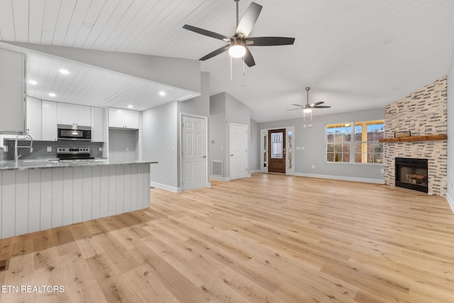 unfurnished living room featuring light wood-type flooring, a brick fireplace, ceiling fan, and vaulted ceiling