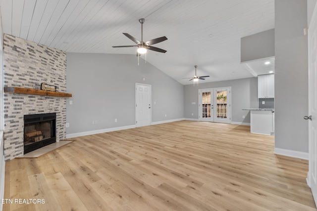 unfurnished living room featuring ceiling fan, french doors, lofted ceiling, a fireplace, and light wood-type flooring