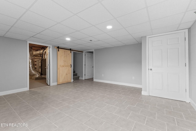 basement with a paneled ceiling, a barn door, and light tile patterned flooring