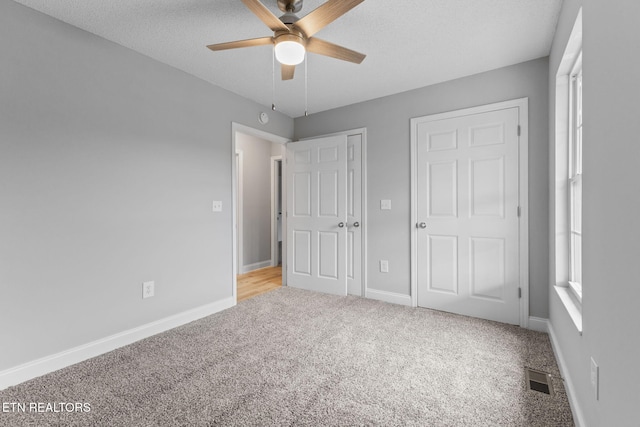 unfurnished bedroom featuring multiple closets, ceiling fan, light colored carpet, and a textured ceiling