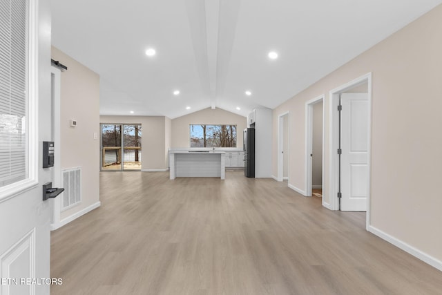 unfurnished living room featuring a barn door, light hardwood / wood-style flooring, and vaulted ceiling