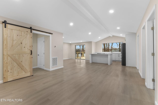 unfurnished living room with light wood-type flooring, a barn door, and vaulted ceiling