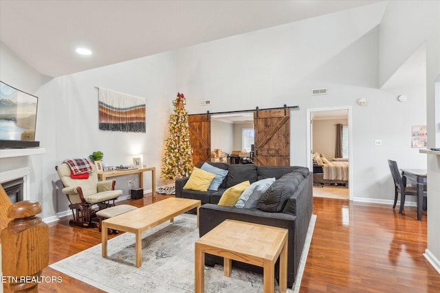 living room with wood-type flooring, a barn door, and high vaulted ceiling