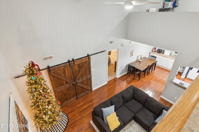 living room with hardwood / wood-style flooring, ceiling fan, a barn door, and a high ceiling