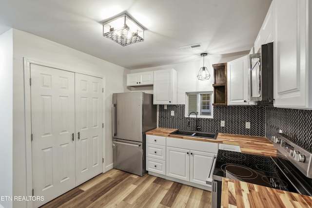 kitchen with sink, stainless steel appliances, wooden counters, decorative light fixtures, and white cabinets