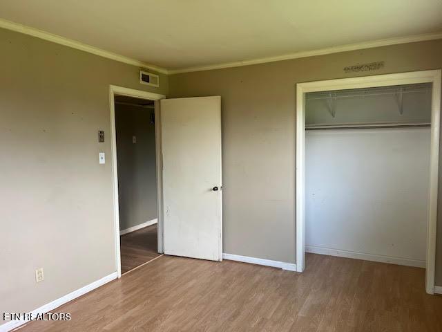 unfurnished bedroom with wood-type flooring, a closet, and crown molding