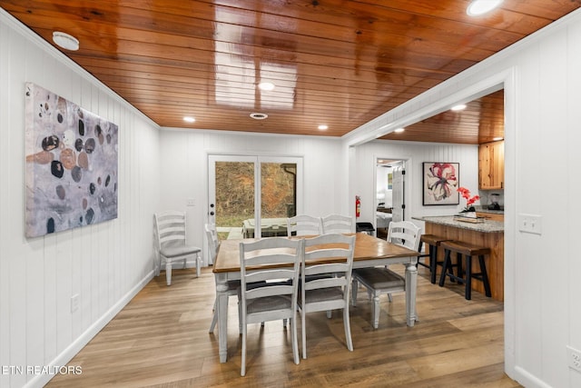 dining room with wood walls, wooden ceiling, crown molding, and light hardwood / wood-style flooring