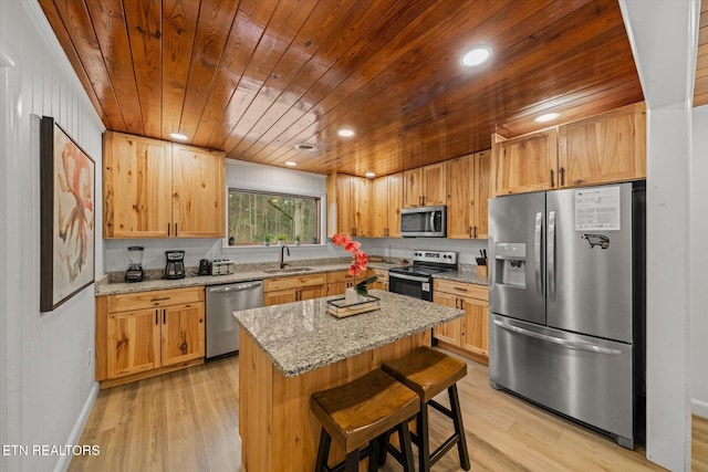 kitchen featuring light stone countertops, a kitchen breakfast bar, stainless steel appliances, sink, and a kitchen island