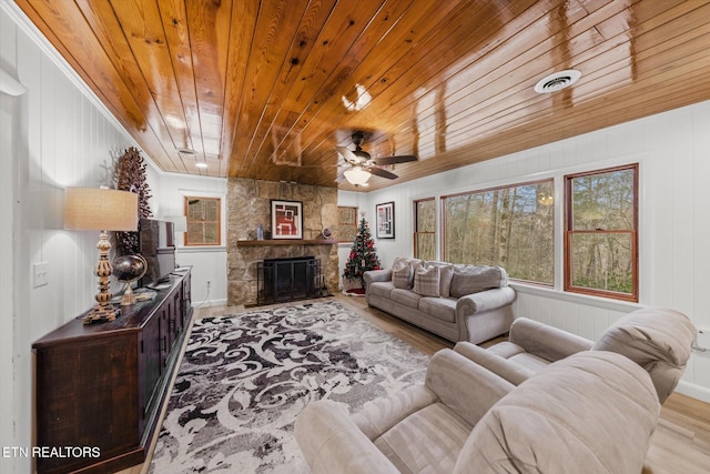 living room featuring ceiling fan, a stone fireplace, wooden ceiling, and light wood-type flooring