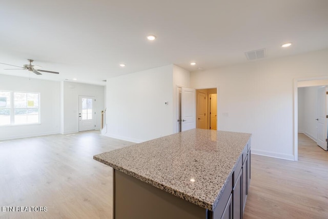 kitchen with light hardwood / wood-style floors, a center island, ceiling fan, and light stone counters