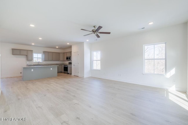 unfurnished living room with sink, ceiling fan, a healthy amount of sunlight, and light hardwood / wood-style flooring