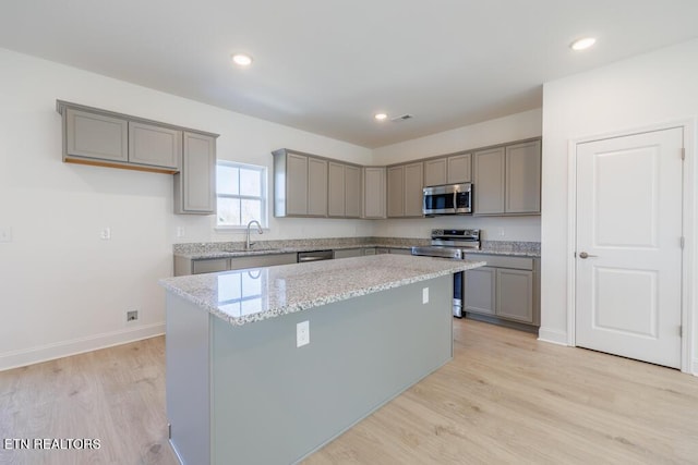 kitchen featuring a center island, stainless steel appliances, sink, light wood-type flooring, and light stone counters