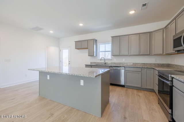 kitchen featuring light stone countertops, a kitchen island, appliances with stainless steel finishes, and gray cabinets