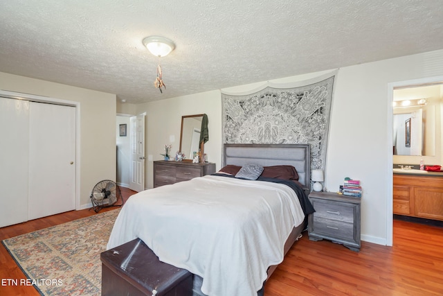 bedroom with ensuite bath, a textured ceiling, sink, wood-type flooring, and a closet