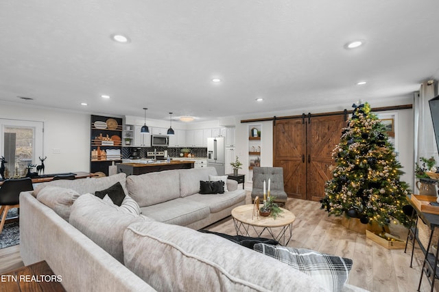 living room featuring a barn door, light hardwood / wood-style floors, sink, and ornamental molding