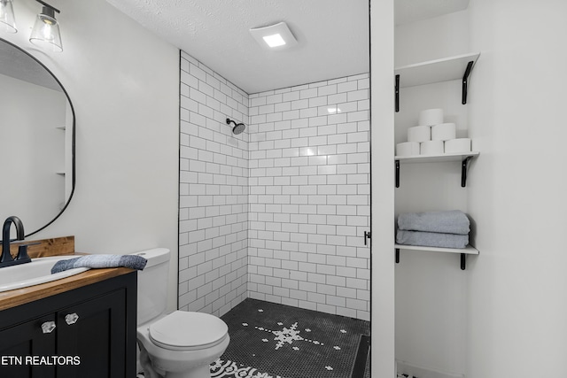 bathroom featuring vanity, a tile shower, a textured ceiling, and toilet