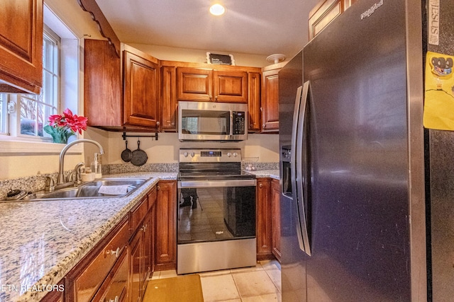 kitchen featuring light stone counters, sink, light tile patterned floors, and stainless steel appliances