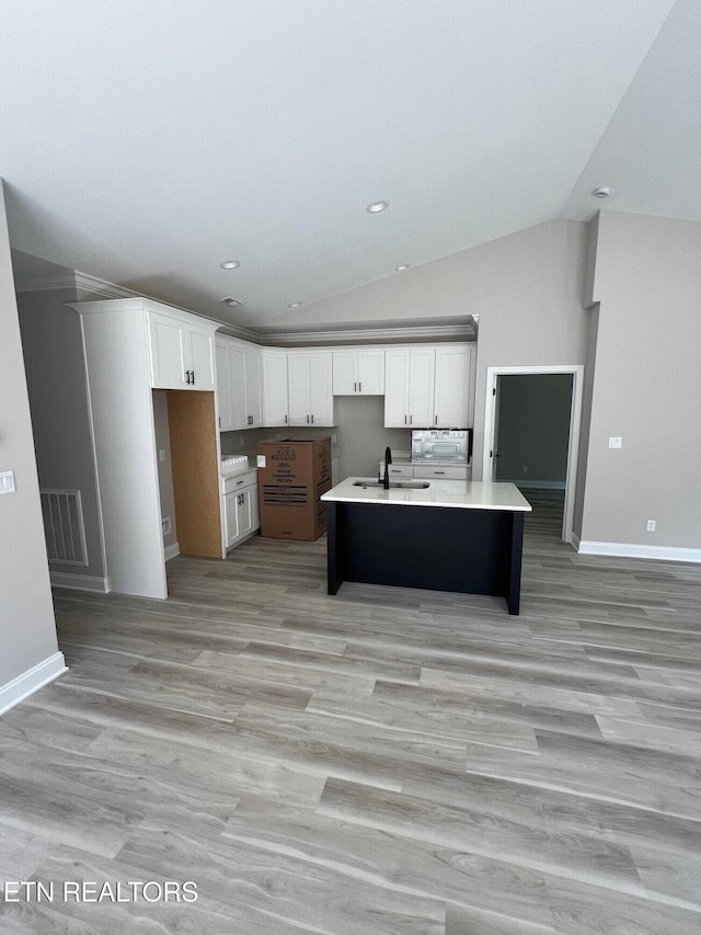 kitchen with vaulted ceiling, a kitchen island with sink, sink, white cabinets, and light hardwood / wood-style floors