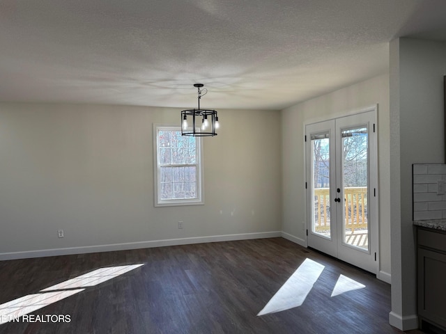 unfurnished dining area featuring dark hardwood / wood-style floors, a wealth of natural light, a textured ceiling, and french doors